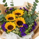 Bouquet of sunflowers, purple statice, eucalyptus, and small white flowers.