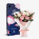 A white and pink rose bouquet in a vase with a pink ribbon, next to a blue box with floral design.