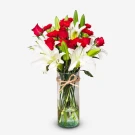 Red roses, white lilies, and red carnations in a clear vase tied with twine.