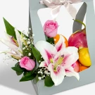 A gift box filled with pink roses, white lilies, dragon fruit, oranges, and lemons.