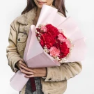 Woman holding a bouquet of red and pink carnations wrapped in pink paper.