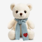 Cream teddy bear wearing a blue knitted scarf with a red heart patch.