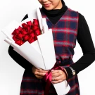 Woman in plaid dress holding a large bouquet of 18 red roses.