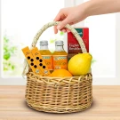 Wicker basket with orange juice, lemon, orange, tea box, and mini straws, held by a hand.