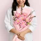 Woman holding a bouquet of pink gerbera daisies wrapped in pastel pink paper.