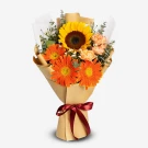 A bouquet of sunflowers, orange gerberas, and yellow carnations wrapped in brown paper with a burgundy ribbon.