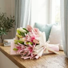 Pink lilies in a bouquet with pink and beige wrapping, tied with a cream ribbon.