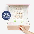 Pink gift box with pop-up birthday cake and "Happy Birthday" text.