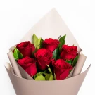 Six red roses with green leaves, wrapped in beige paper.