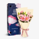 Pink lilies and carnations in a cream-colored bouquet with a pink ribbon.