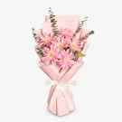 Pink gerbera daisy bouquet wrapped in pastel pink paper, tied with a white ribbon.