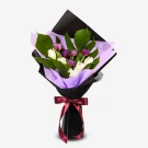 Bouquet of violet tulips with greenery, wrapped in black and purple paper, tied with a red ribbon.