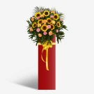 Tall red vase holding a vibrant bouquet of sunflowers, pink and orange carnations, and greenery.
