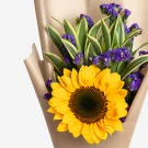 Sunflower with purple statice and green leaves, wrapped in brown paper.