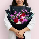 Woman holding Sweetened Love bouquet: red and white roses, violet statice, eucalyptus, dark wrapper.