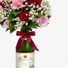 Bouquet of pink and red roses and carnations in a green sparkling apple juice bottle with a red ribbon.
