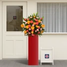 Tall red stand with vibrant orange gerberas and pink carnations, next to a white A-frame sign with a logo.