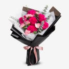 Bouquet of bright pink roses and pink carnations with eucalyptus, wrapped in black paper and tied with a pink ribbon.