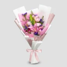 Pink stargazer lilies, roses, and purple statice in a bouquet wrapped in pink and white paper with a pink ribbon.
