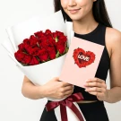 Woman holding a bouquet of red roses and a card with "LOVE" inside a heart made of roses.