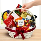 White wicker gift basket filled with chocolates, biscuits, and other gourmet treats, tied with a red bow.
