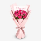 Bouquet of 12 pink roses wrapped in pink paper with a pink ribbon, featuring a card that says "I love you!".