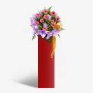 A red pedestal holds a large bouquet of pink gerberas and greenery with a yellow ribbon.
