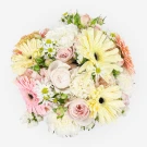 A round bouquet of soft pink and yellow gerbera daisies, roses, carnations, and small white daisies.
