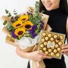 Woman holding a bouquet of sunflowers and a box of Ferrero Rocher chocolates.