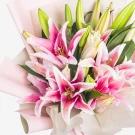 Pink stargazer lilies in a bouquet with green buds and pink and cream wrapping.