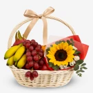 Fruit basket with sunflower, bananas, grapes, dragonfruit, apple, and orange, tied with a ribbon.