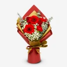 A bouquet of red gerberas, roses, and carnations with baby's breath, wrapped in red and gold paper.