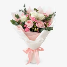 A bouquet of pink and white roses, pink carnations, and eucalyptus, wrapped in white and pink paper with a pink ribbon.