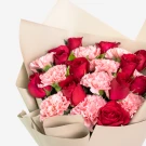 Bouquet of red roses and pink carnations, wrapped in neutral paper.