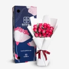Pink roses in white paper bouquet next to a floral gift box with pink and blue patterns.