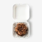 Chocolate cake with chocolate frosting and sprinkles in a white takeout box.