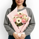 Woman in gray sweater holding a pink and white flower bouquet with a white ribbon.