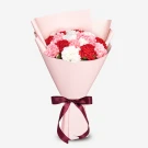 Bouquet of red, pink, and white carnations in pink paper with a burgundy ribbon.
