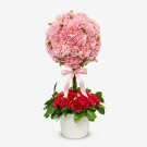 Pink and red carnation topiary with pink bow and lights in a white pot.