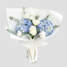Blue hydrangeas and white roses in a white bouquet with eucalyptus and a ribbon.