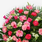 A lush arrangement of pink roses, carnations, and gerberas with green foliage.