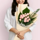 Woman holding a bouquet of pink spray roses in cream paper wrap.
