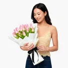 A bouquet of 20 pink tulips wrapped in white paper and tied with a black ribbon.