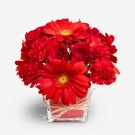 A compact glass vase filled with red roses, carnations, and gerbera daisies tied with twine.