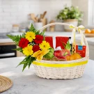 Wicker basket with flowers, fruit, and Dilmah tea on a countertop.