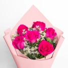 Six vibrant pink roses and white filler flowers arranged in a pale pink paper bouquet.
