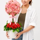 Woman holds a pink carnation topiary with red carnations at the base in a white pot.