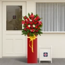 Grand opening flower arrangement with red anthuriums, roses, gerberas, mums, and carnations in a tall red vase.