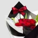 A bouquet of red roses and white tulips wrapped in black and white paper, tied with a red ribbon.
