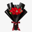 A bouquet of 12 red roses with eucalyptus and ruscus leaves, wrapped in black paper and tied with a burgundy ribbon.